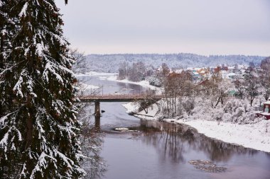 Kış kırsal arazisi. Nehir kıyısında karla kaplı bir köy bir yol köprüsü tarafından geçiliyor..