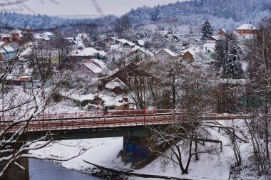 Kış kırsal arazisi. Nehir kıyısında karla kaplı bir köy bir yol köprüsü tarafından geçiliyor..