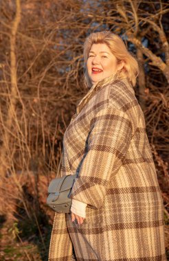 Parlak bir sonbahar gününde, parktaki ekose ceketli, sarışın, tombul bir kadının portresi..