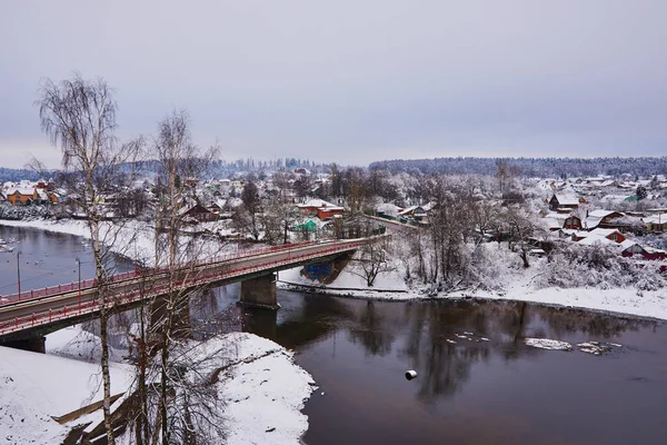 Village enneigé au bord d'une rivière traversé par un pont routier. — Photo