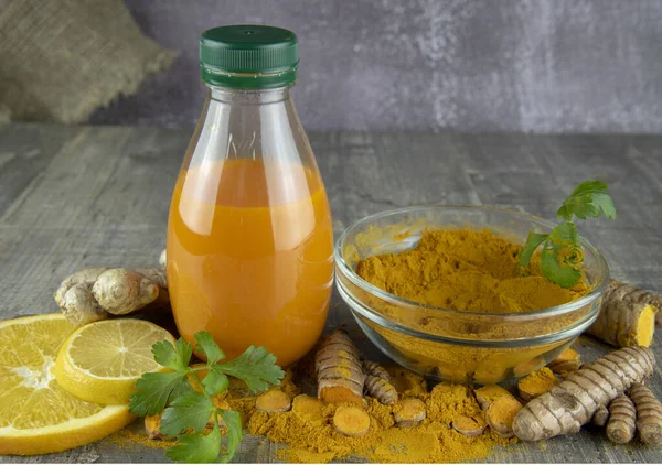 Turmeric juice in a bottle, ginger, lemon, orange and turmeric powder on a wooden background.