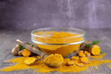 Gri arka planda şeffaf bir kasede taze zerdeçal kökü ve zerdeçal tozu. Yiyecek takviyeleri, sağlıklı yiyecekler..