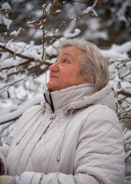 Kışın kar ormanlarında yürüyüş yapan açık renk ceketli yaşlı bir kadın..