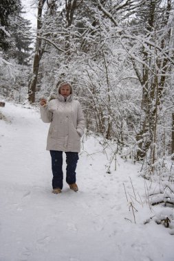 Kışın kar ormanlarında yürüyüş yapan açık renk ceketli yaşlı bir kadın..