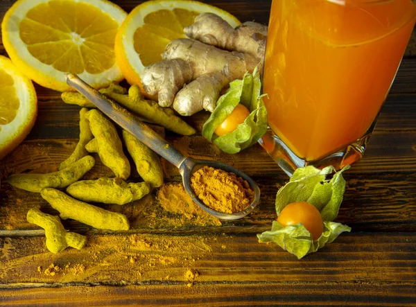 Tahta zemin üzerinde zerdeçal tozu, kurutulmuş zerdeçal kökü, zencefil, turunçgil ve vitamin suyu..