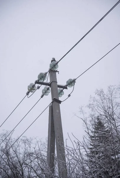 Power line sprinkled with snow against the background of a cloudy sky on a winter day.