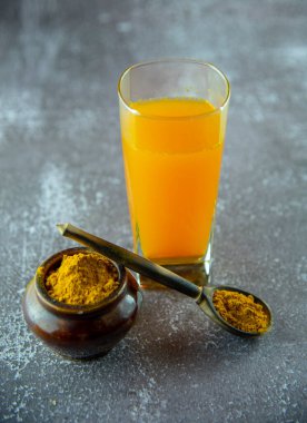 Küçük bir çömlekte zerdeçal tozu ve bir tahta kaşık ve gri arka planda bir bardak meyve suyu..