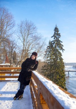 Kızıl saçlı orta yaşlı bir kadın, siyah kürk giyiyor, güneşli bir günde, arka planda bir kış manzarasına karşı..