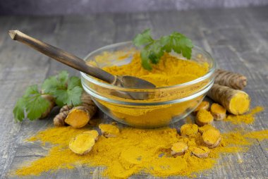 Gri arka planda şeffaf bir kasede taze zerdeçal kökü ve zerdeçal tozu.. 