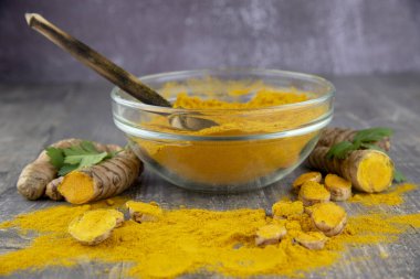 Gri arka planda şeffaf bir kasede taze zerdeçal kökü ve zerdeçal tozu.. 