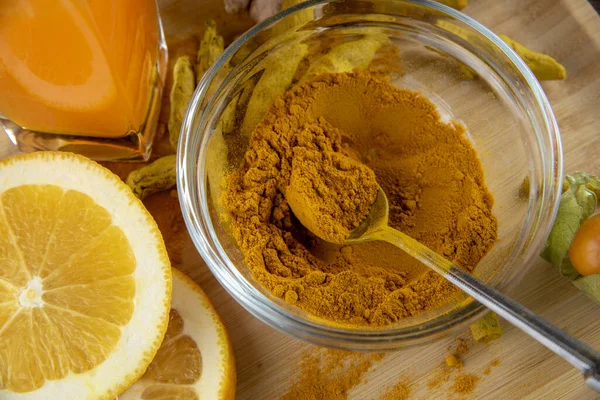 Polvo de cúrcuma en un recipiente de vidrio y un vaso de jugo en una bandeja de madera. —  Fotos de Stock