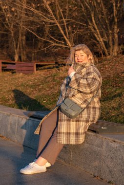 Dolgun, orta yaşlı sarışın bir kadının portresi güneşli bir sonbahar gününde parkta yürüyor..