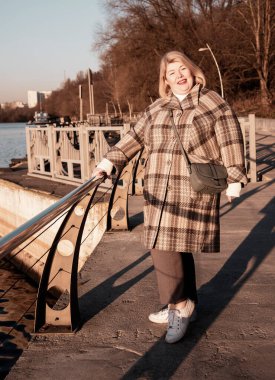 Dolgun, orta yaşlı sarışın bir kadının portresi güneşli bir sonbahar gününde parkta yürüyor..