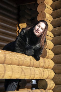 Orta yaşlı bir kadın ahşap bir evin penceresinden dışarı bakar. Doğada fotoğraf çekimi..