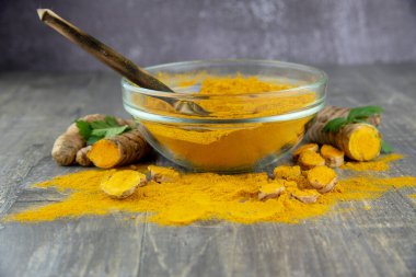 Gri arka planda şeffaf bir kasede taze zerdeçal kökü ve zerdeçal tozu. Yiyecek takviyeleri, sağlıklı yiyecekler..