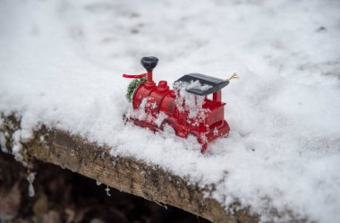 Küçük kırmızı bir oyuncak tren pofuduk karda duruyor..