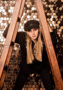  Siyah elbiseli genç bir kız altın bir duvara karşı merdiveni tutuyor..