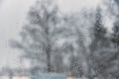 Bulanık kış manzarası. Islak arabanın camından, ağaçların bulanık siluetlerini görebilirsin..