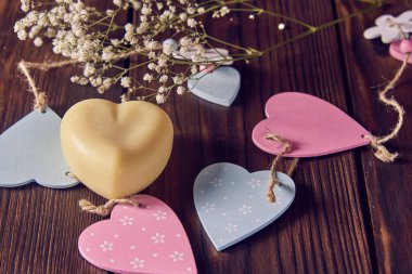 Kalp şeklinde el yapımı mis kokulu bir sabun. Arkaplanda ahşap bir dekor ve çiçekler var..