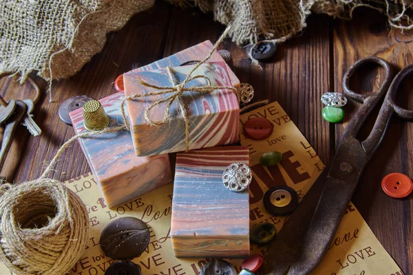 Scented organic handmade soap and packaging materials lie on a dark wooden table.