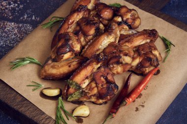 Servis tahtasının üzerinde çeşitli baharatlar, otlar ve sebzelerle süslenmiş lezzetli kızarmış tavuk kanatları var. Seçici odak.