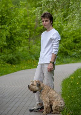 Beyaz elbiseli genç bir adam bir bahar günü şehir parkında bir köpekle yürür..