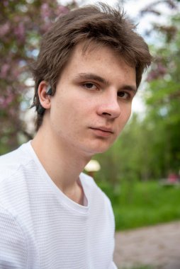 Bahar doğasının arka planına karşı beyaz tişörtlü 18 yaşındaki bir çocuğun portresi.