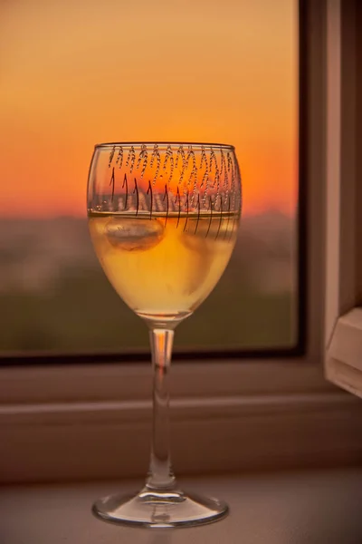 Una copa de vino en el alféizar de la ventana sobre el fondo de la puesta de sol. — Foto de Stock