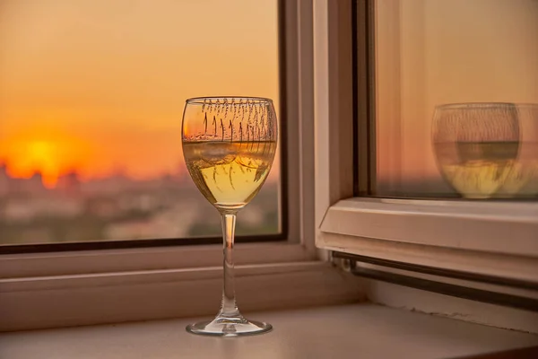 Una copa de vino en el alféizar de la ventana sobre el fondo de la puesta de sol. — Foto de Stock
