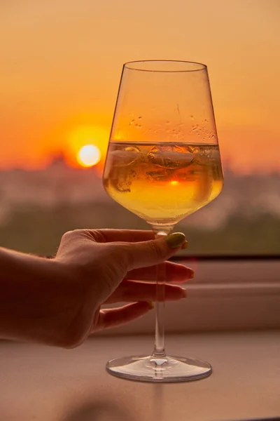 Una mano de mujer con una copa de vino en el fondo de una puesta de sol brillante. — Foto de Stock