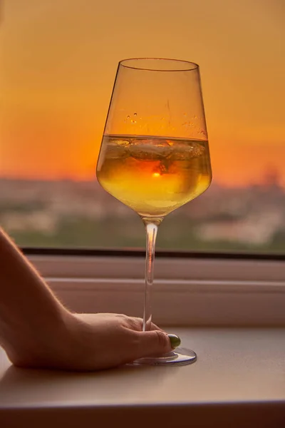 Una mano de mujer con una copa de vino en el fondo de una puesta de sol brillante. — Foto de Stock