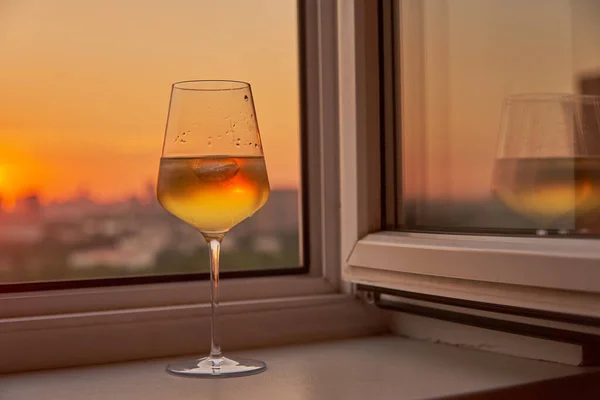 Una copa de vino en el alféizar de la ventana sobre el fondo de la puesta de sol. — Foto de Stock