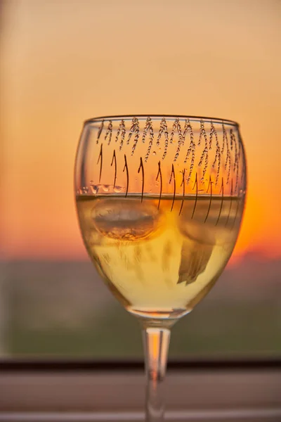 A glass of white wine on the windowsill against the background of the sunset.