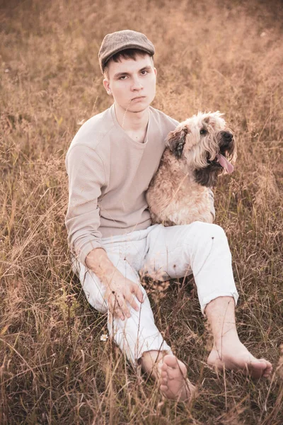 Un garçon de 18 ans dans une casquette est assis avec un chien sur un terrain . — Photo