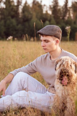 18 yaşında kepli bir çocuk bir yaz akşamında çimlerin üzerinde bir köpekle oturuyor..