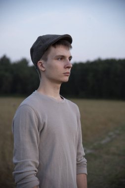 18 yaşında şapkalı bir çocuğun portresi, tarlanın ortasında toprak bir yolda duruyor..
