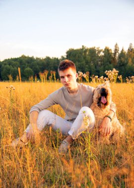 18 yaşında bir çocuk, bir yaz akşamında çimlerin üzerinde bir köpekle oturuyor..