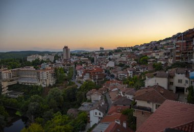 Kırmızı kiremitli çatıları olan evler, yumuşak bir günbatımının arka planına karşı bir dağın üzerine inşa edilmiş. Bulgaristan 'da güzel bir yaz gününde Veliko Tarnovo