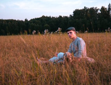 18 yaşında kepli bir çocuk bir yaz akşamında çimlerin üzerinde bir köpekle oturuyor..