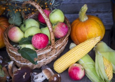Sonbahar hasadı. Hasır sepetteki parlak elmalar ve ahşap bir arka planda çeşitli güz meyveleri ve sebzeler..