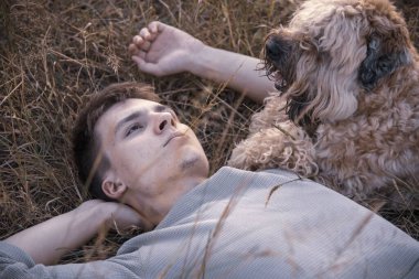 18 yaşında genç bir adamın portresi, bir köpekle yatıyor, yumuşak kaplamalı buğday teriyeri, kuru çimlerin üzerinde, batan güneşin ışınlarında.