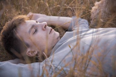 18 yaşında genç bir adamın portresi, kuru çimlerin üzerinde, batan güneşin ışınlarında yatıyor..