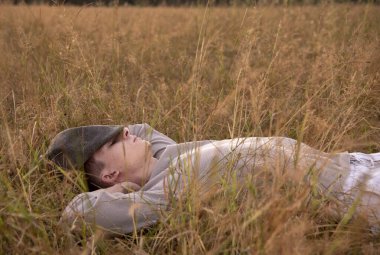 18 yaşında genç bir adamın portresi, kuru çimlerin üzerinde, batan güneşin ışınlarında yatıyor..