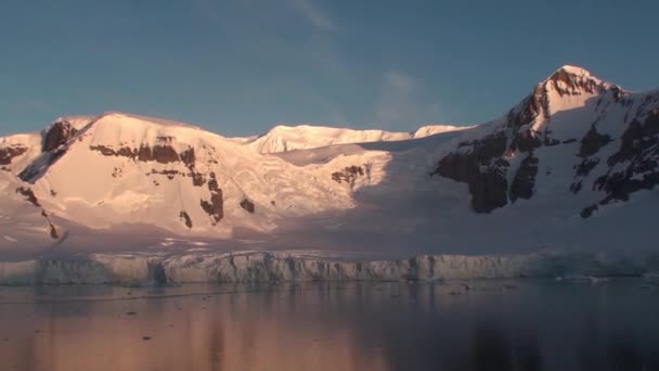 Zonsondergang in Antarctica, met rustig zeewater dat mooi en pittoresk oranje, geel en blauw weerspiegelt en bergen met rotsachtige kusten — Stockvideo
