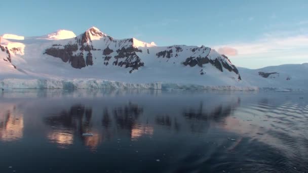 Zonsondergang in Antarctica, met rustig zeewater dat mooi en pittoresk oranje, geel en blauw weerspiegelt en bergen met rotsachtige kusten — Stockvideo