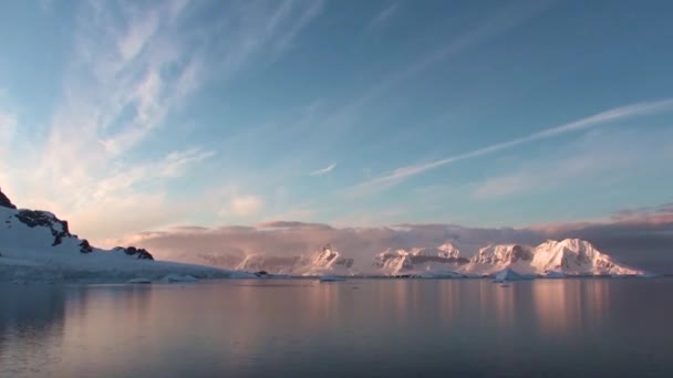 Pôr do sol na Antártida, com águas calmas do mar refletindo laranja bonita e pitoresca, amarelo e azul e montanhas com costas rochosas — Vídeo de Stock