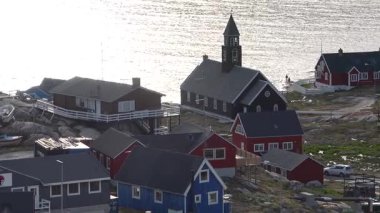 Grönland 'daki ahşap bir kilise, parlak mavi gökyüzünün altında tarihi mimarisini sergiliyor. Binada doğal bir manzaraya sahip yüksek bir kule ve güzel pencereler yer alıyor..
