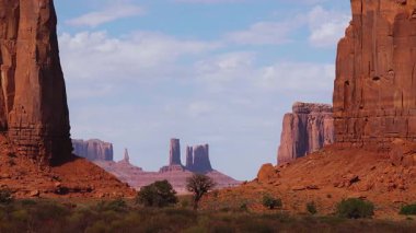Etrafı dağınık bitki örtüsüyle çevrili görkemli kumtaşı oluşumları çöl zemininden yükseliyor. Güneş ışığı, Anıt Vadisi 'ndeki ikonik manzaranın canlı renklerini aydınlatır..