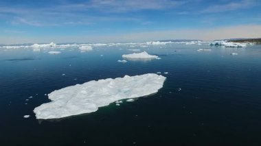 Parlak mavi gökyüzünün altında sakin kutup sularında sürüklenen çarpıcı buzdağlarını keşfedin. Bu nefes kesici Kuzey Kutbu manzarası güzelliği ve buz oluşumlarını gözler önüne seriyor..