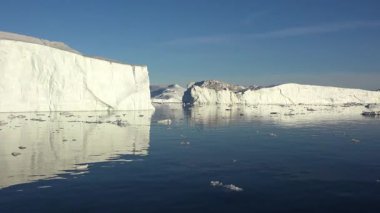 Buzdağları berrak mavi kutup sularında huzur içinde sürüklenirler. Güneş, buzdan yansıyan parlak bir şekilde parlıyor. Kuzey Kutbu 'ndaki doğa harikalarının güzel bir manzarası..